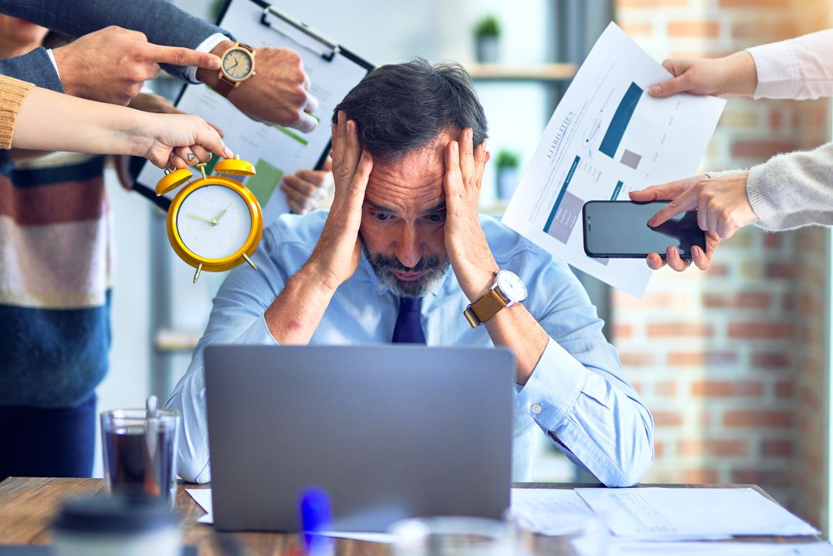 a businessman with head in hands overwhelmed by demands surrounding him
